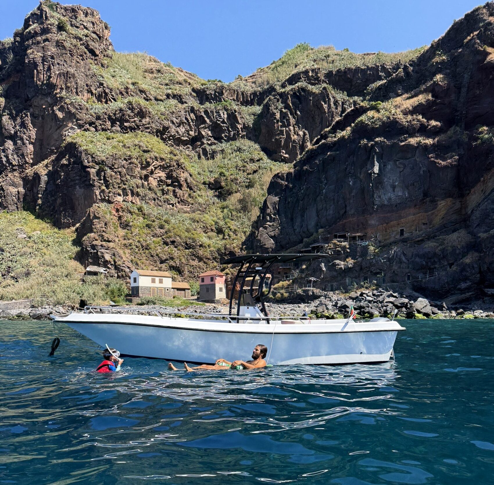 Boa Vida's boat with guests swimming in clear water beneath Madeira's south-coast cliffs